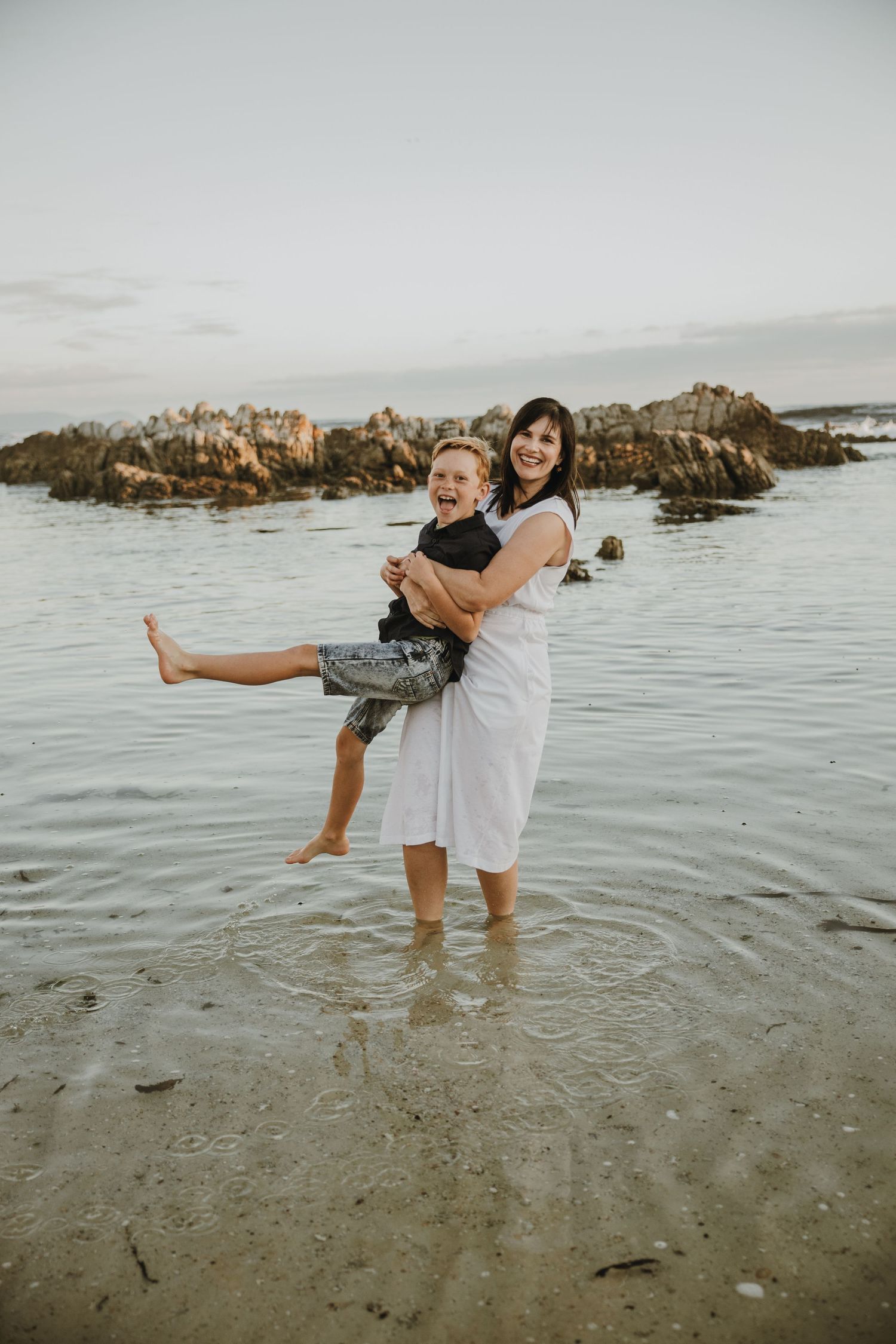 A playful moment captured at the beach with waves and rocky formations in the background.
