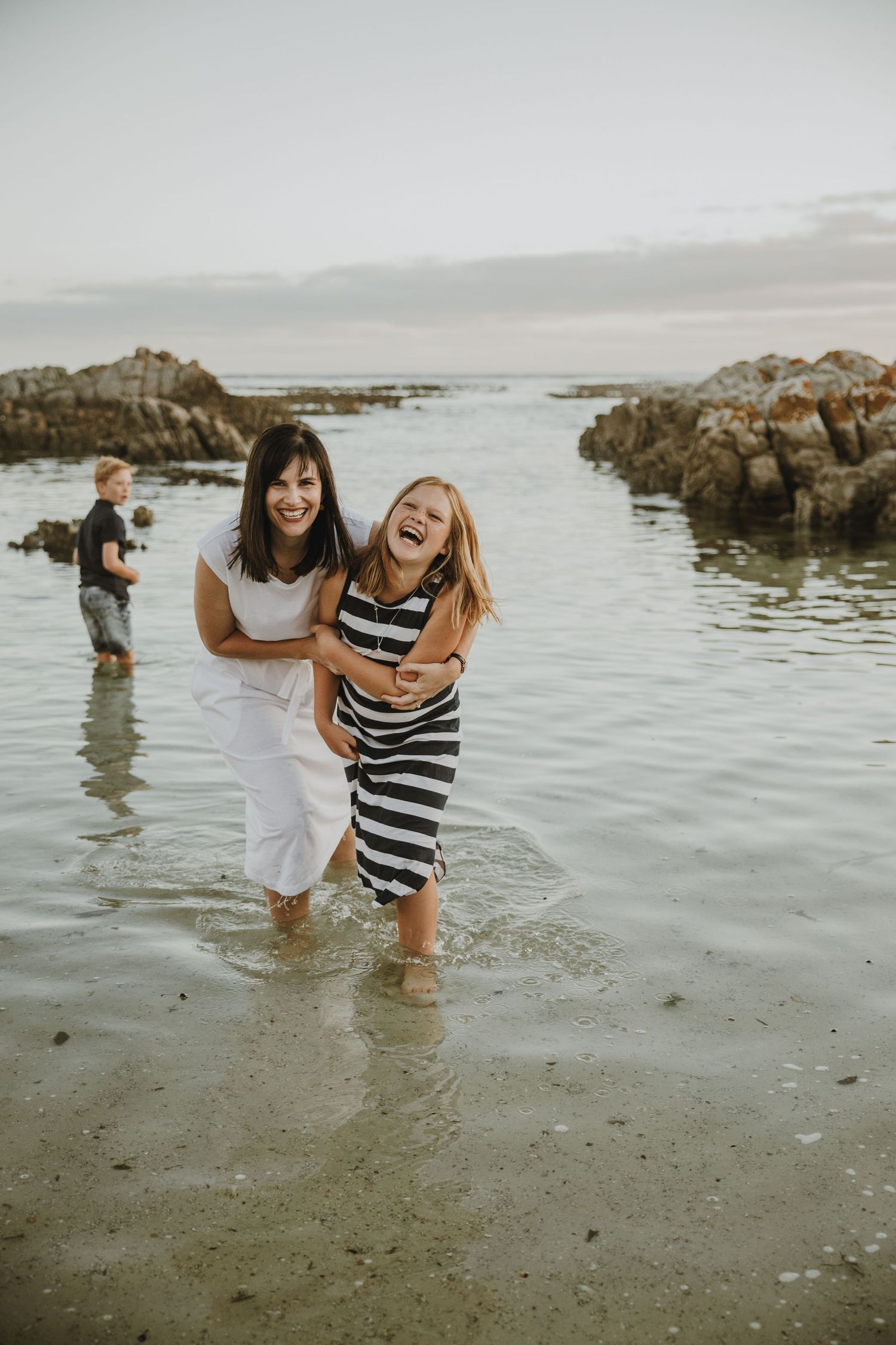 People enjoying the water and laughing together at a rocky beach during golden hour.