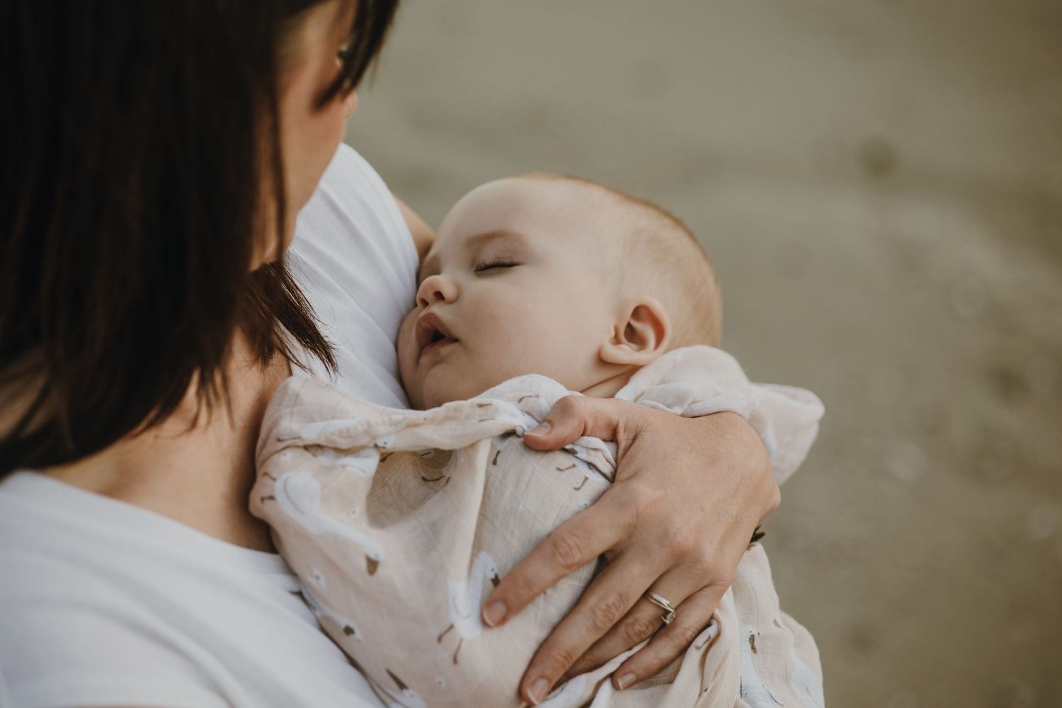 An intimate close-up of a sleeping baby being cradled at the beach.