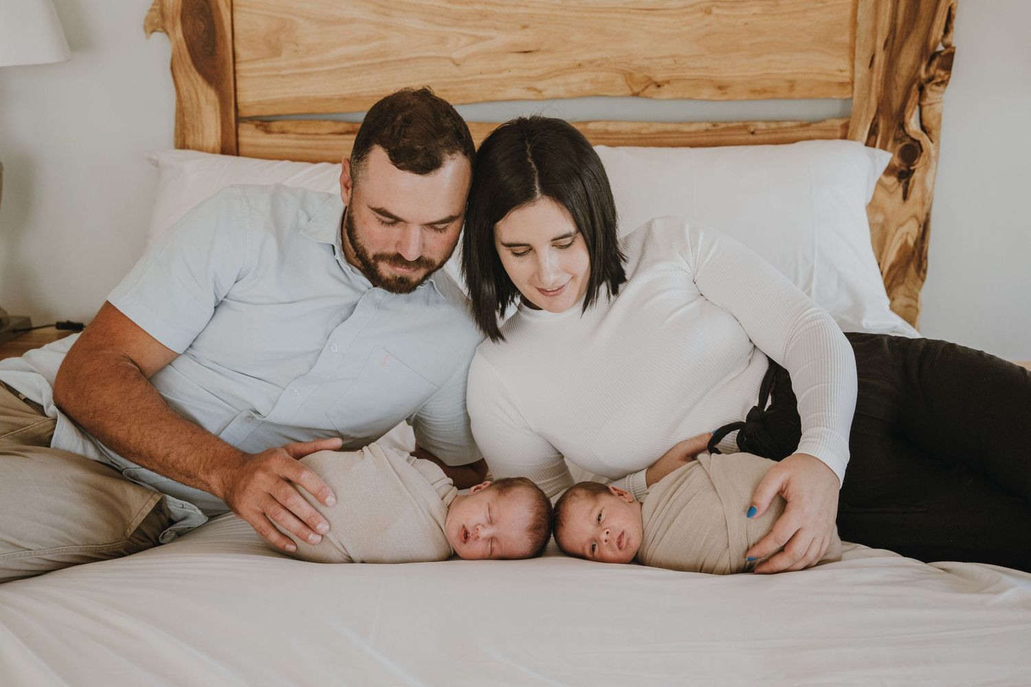 Parents snuggle with their twin babies on a cozy white bed.