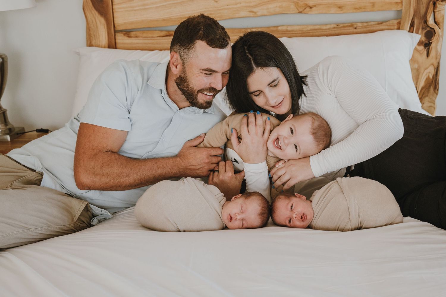 A happy family shares tender moments with their twins on a white bed.