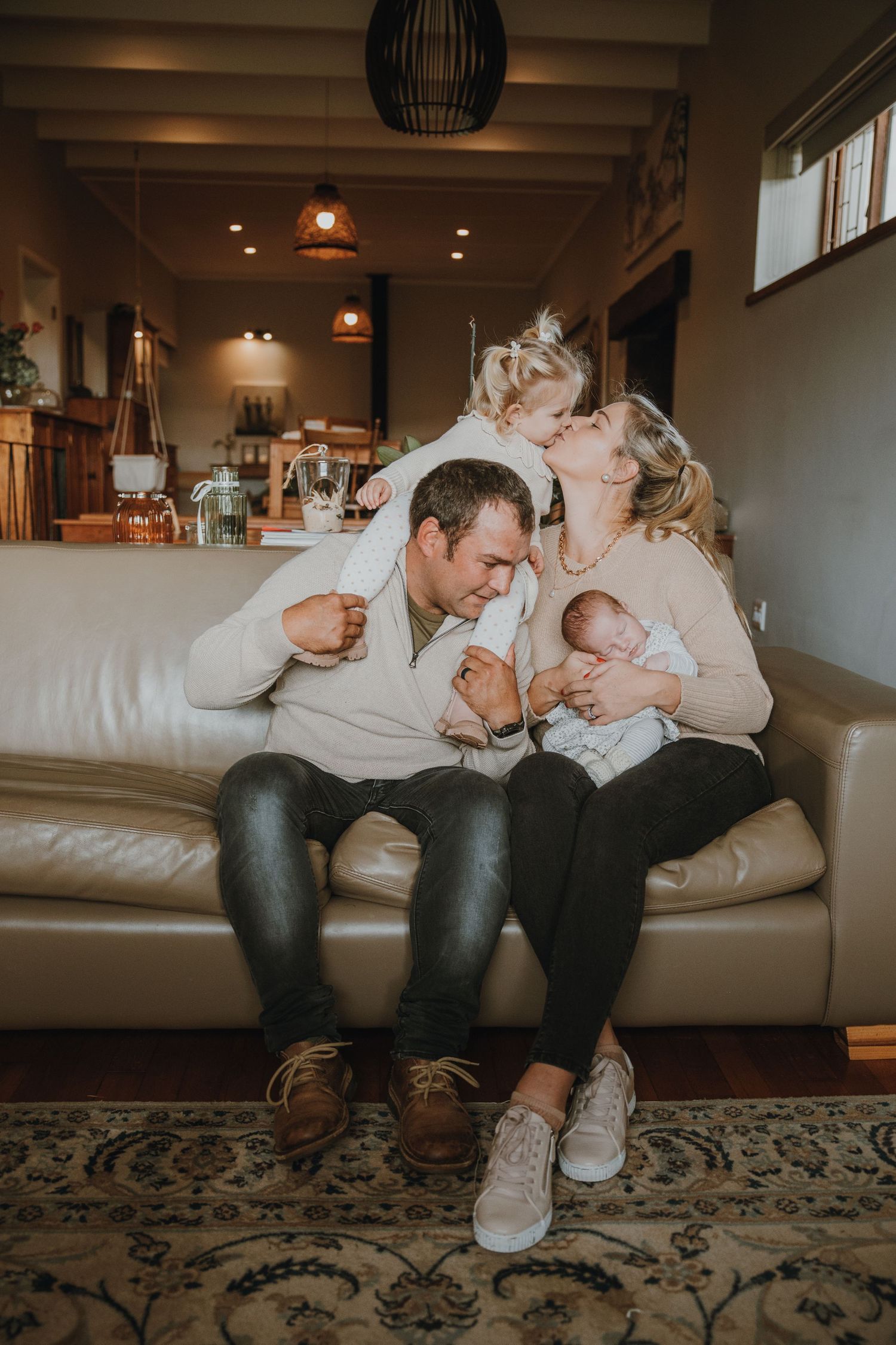 A cozy family moment on a leather couch with a newborn baby in a warm living room setting.