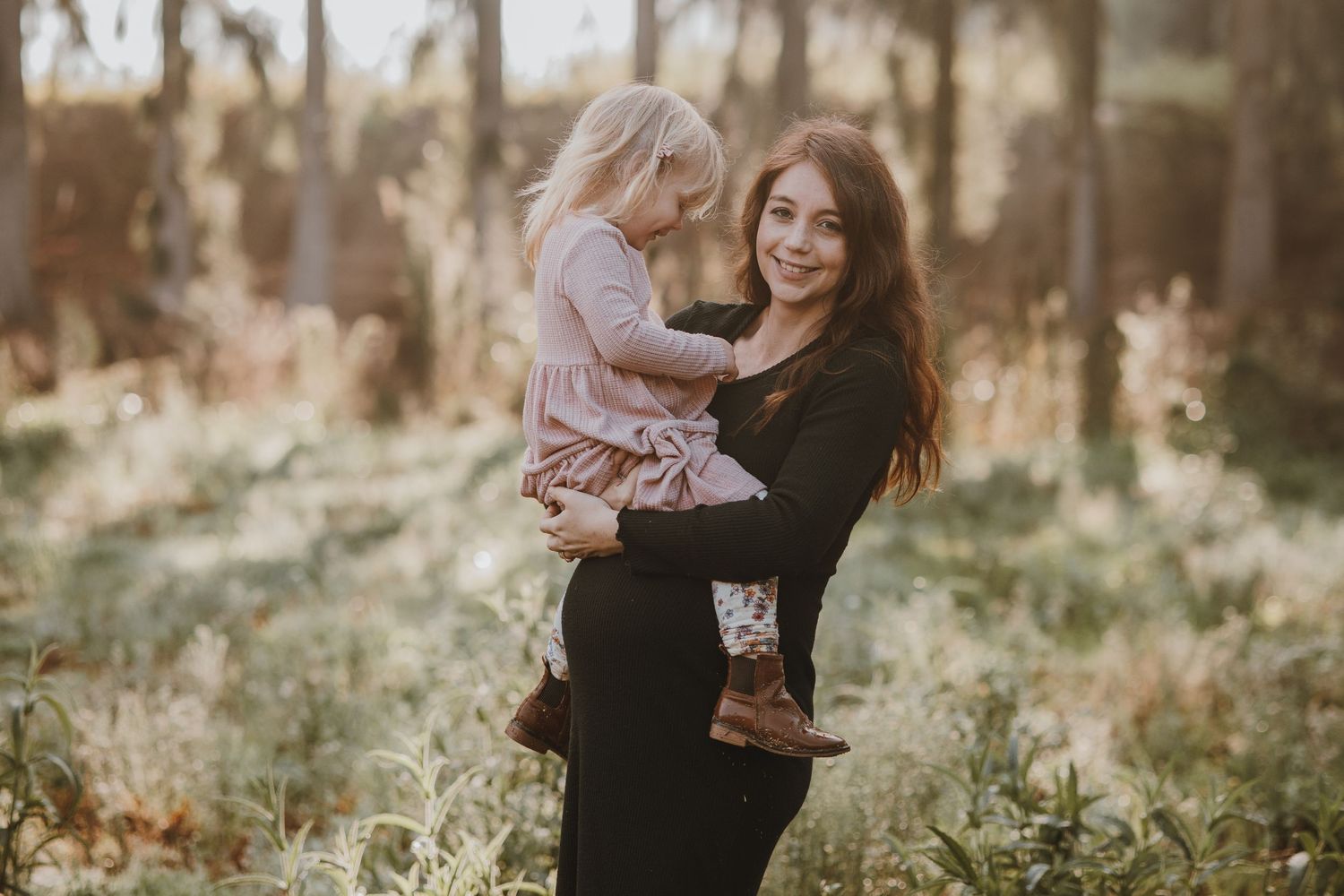 A tender outdoor family moment captured in a wooded setting with golden light.