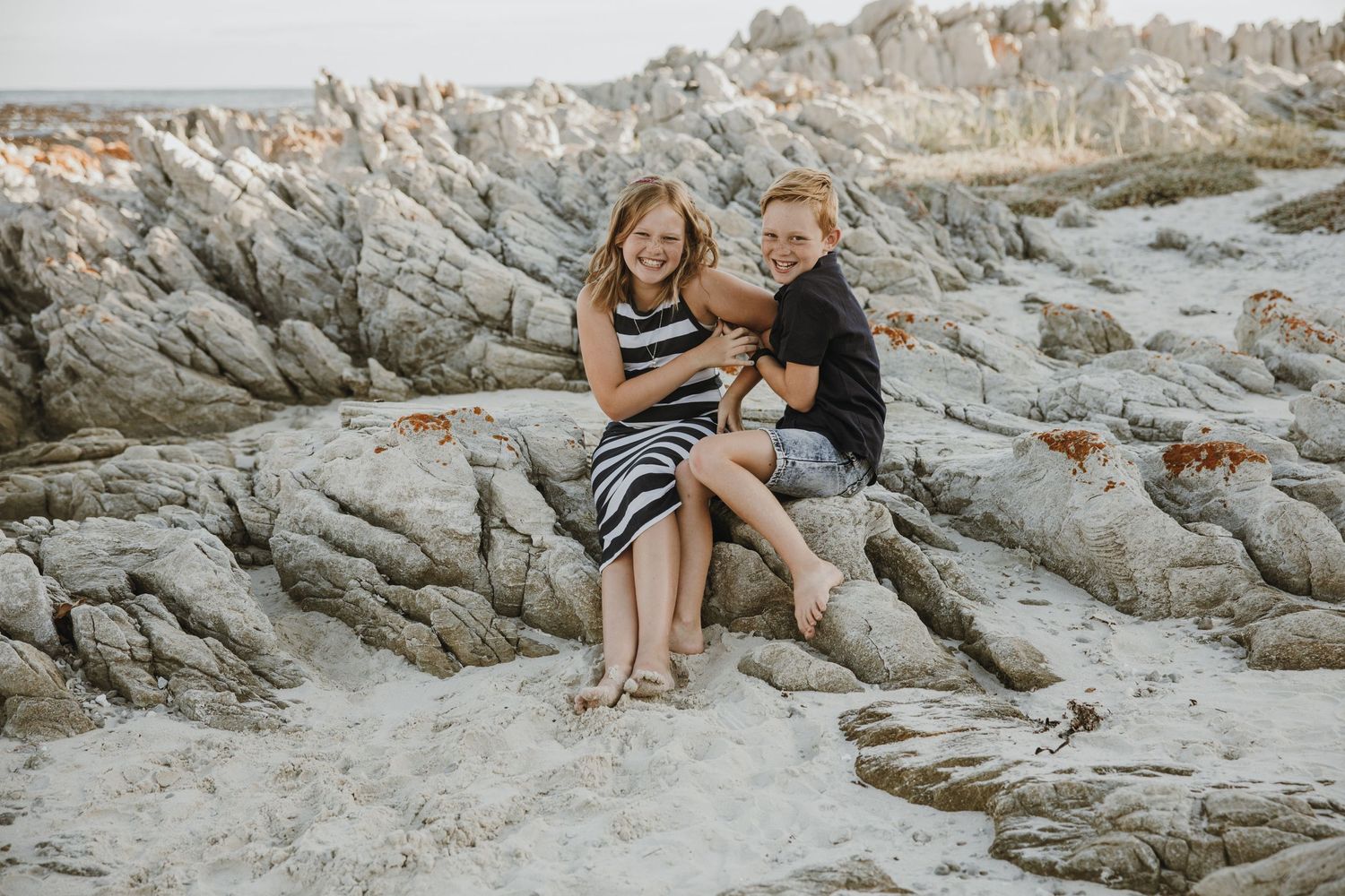 A couple shares a joyful moment while sitting on rugged coastal rocks.
