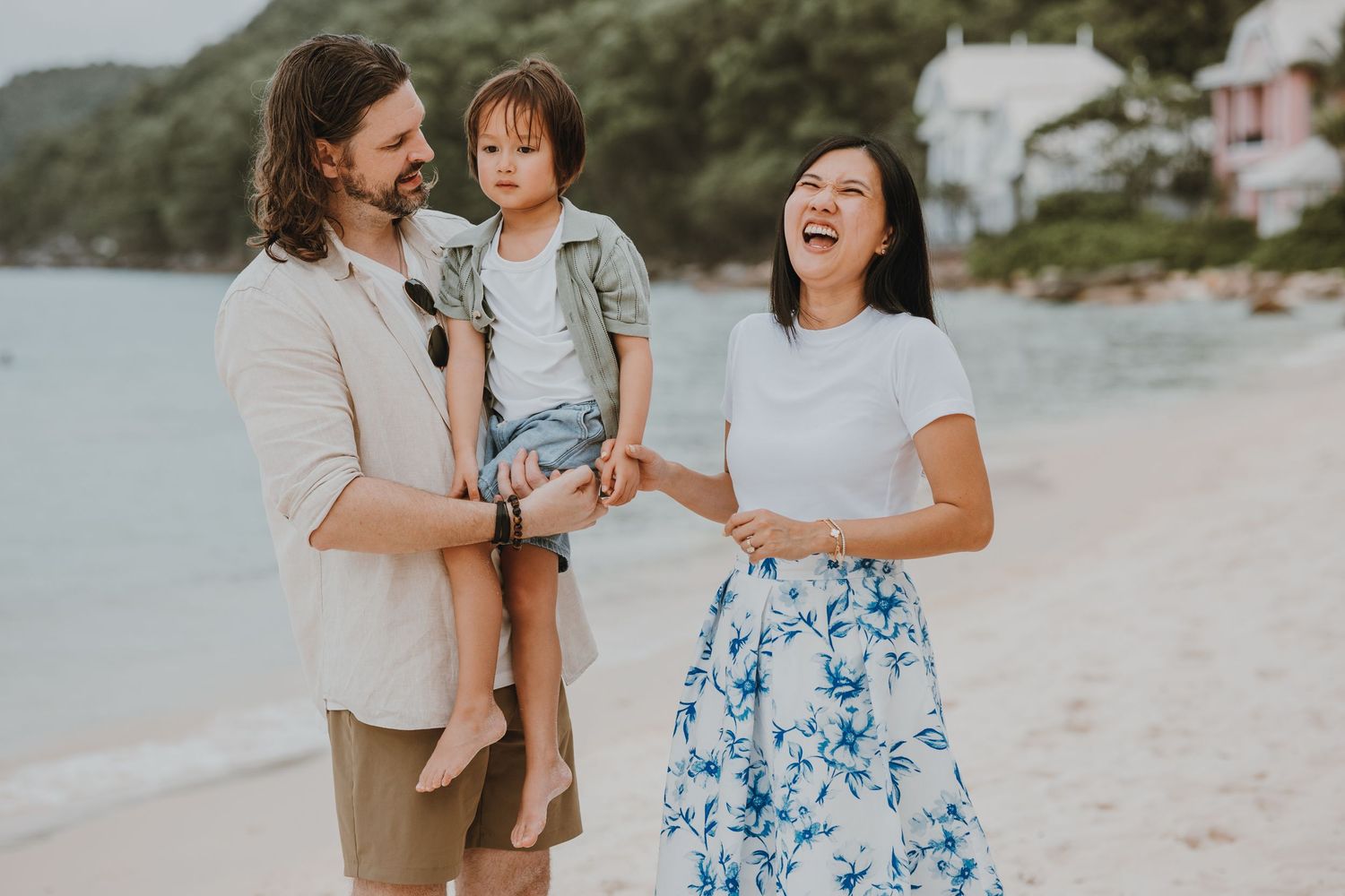 A happy family enjoying a casual stroll together on a beautiful tropical beach with hills in the background.