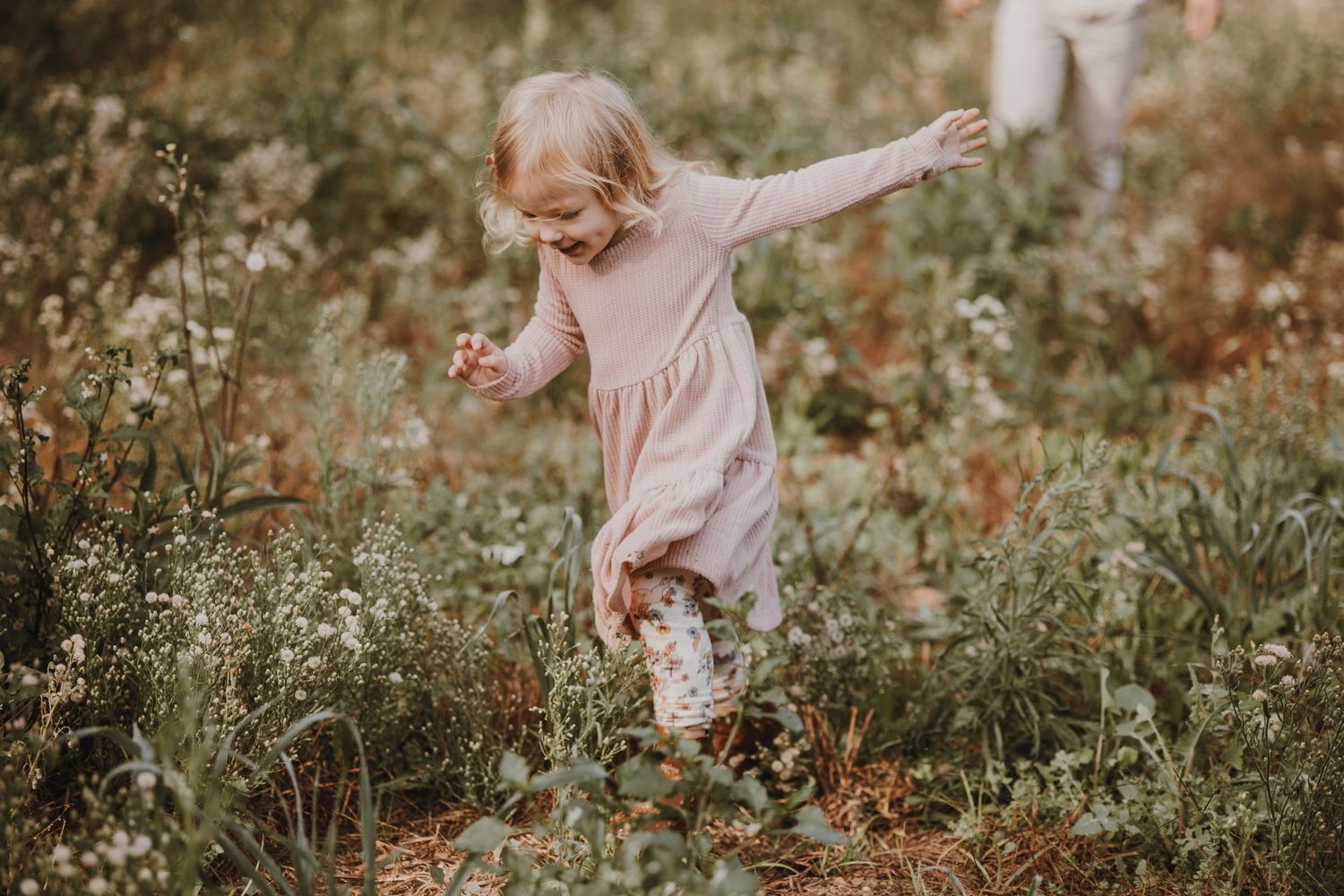 A joyful child running through wildflowers in a pink dress during golden hour.