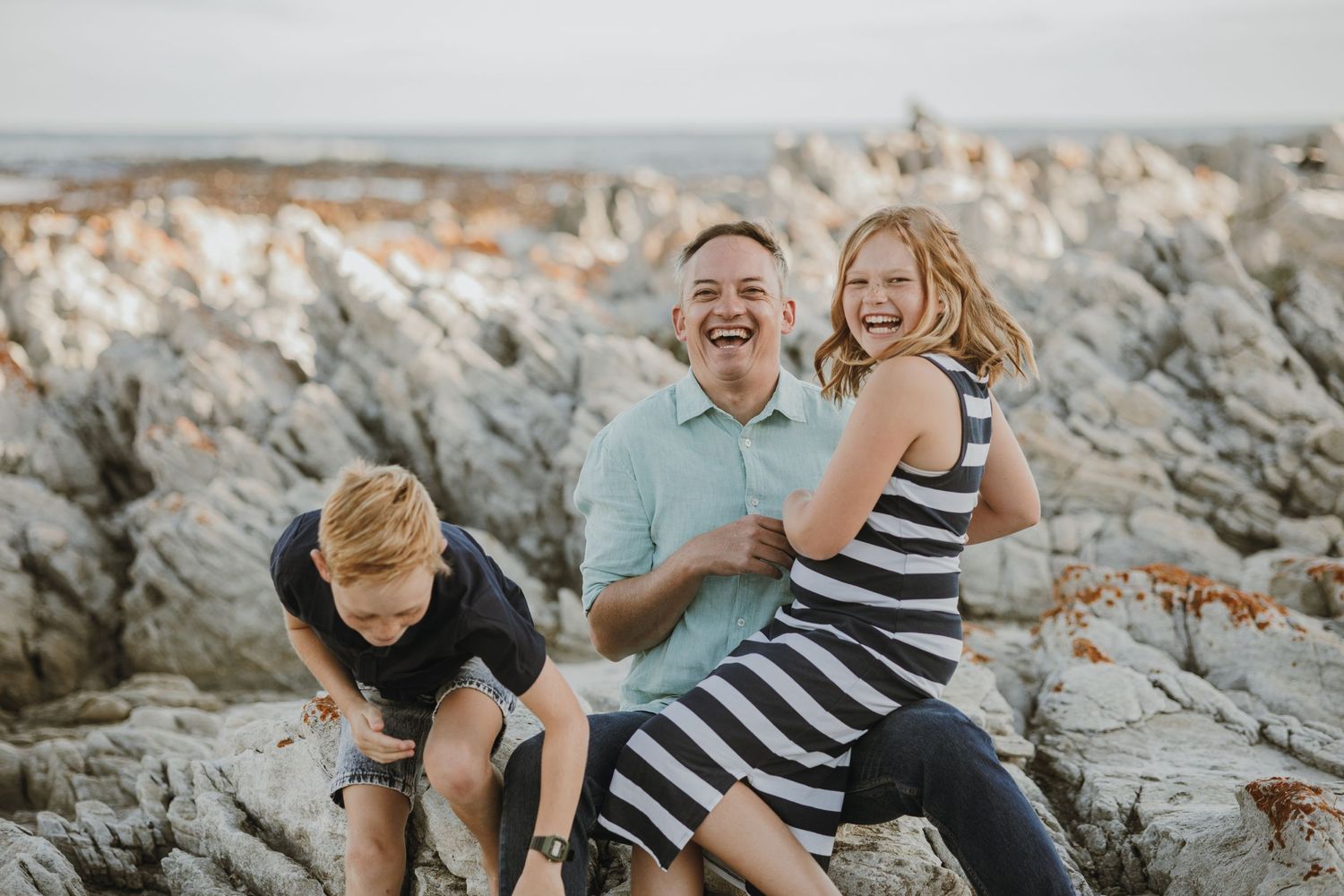 A family shares playful moments together on rocky coastal formations by the ocean.