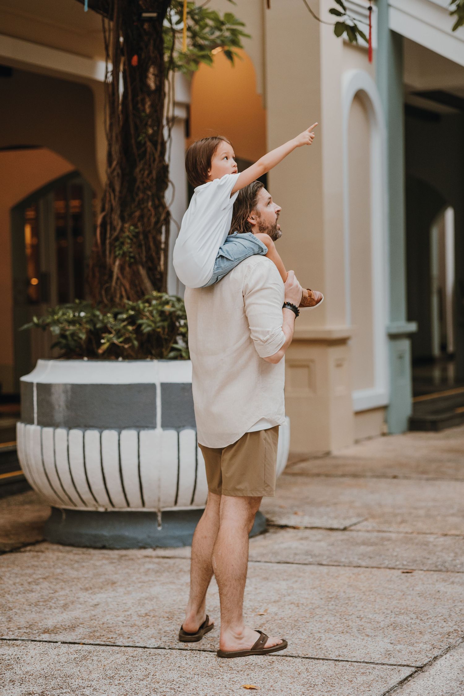 A parent and child share a playful moment outside on a city sidewalk next to a large white planter.