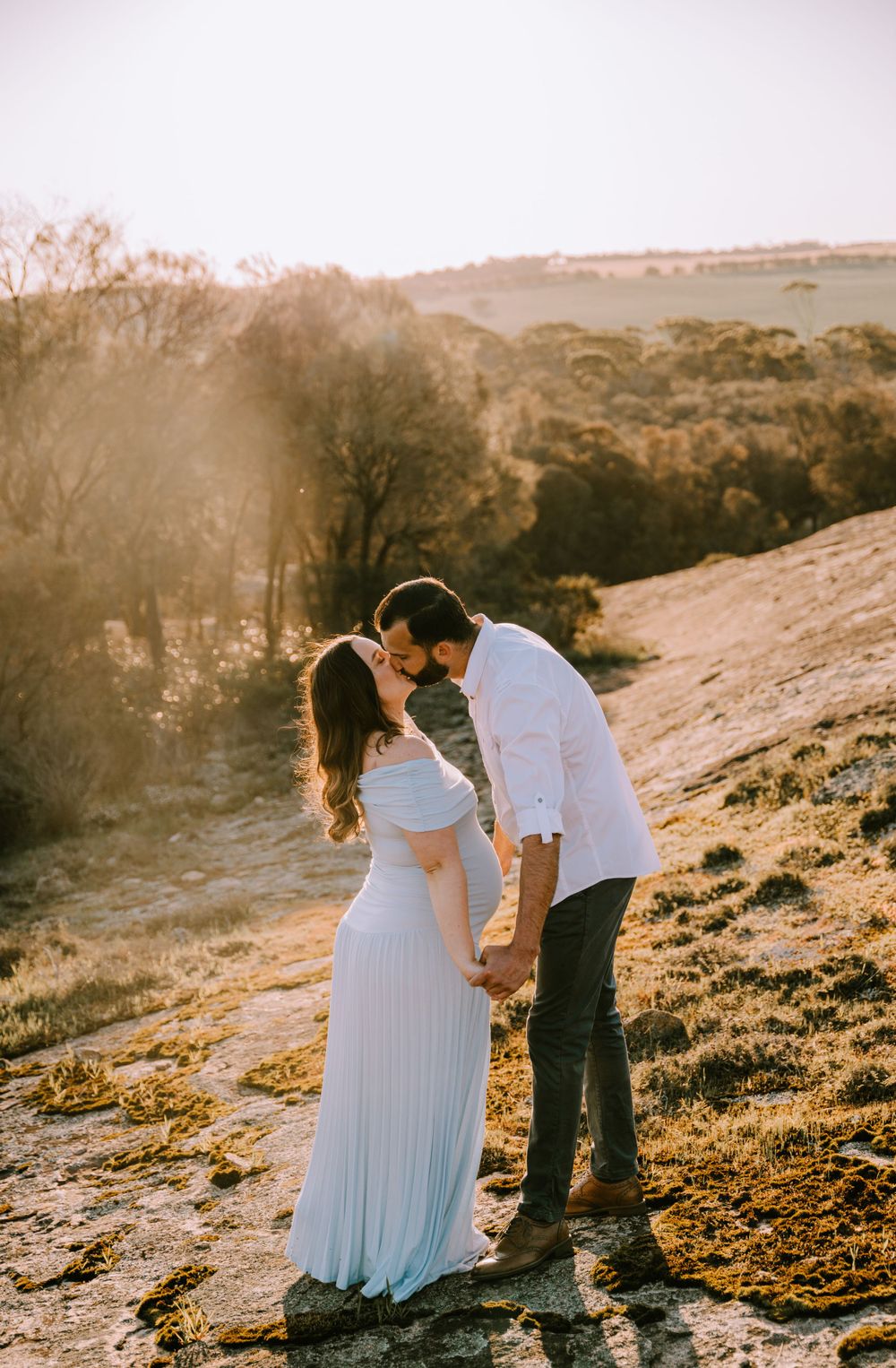 A couple shares a tender moment on a hillside during golden hour.