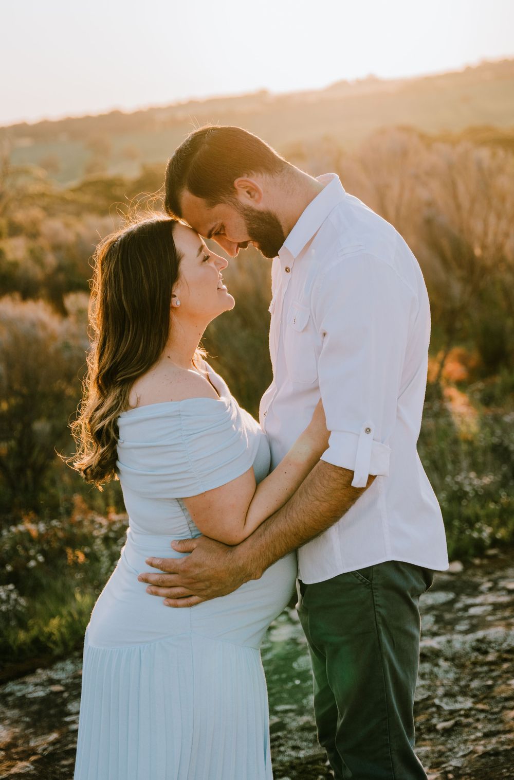 A romantic couple poses together during sunset in an outdoor setting.