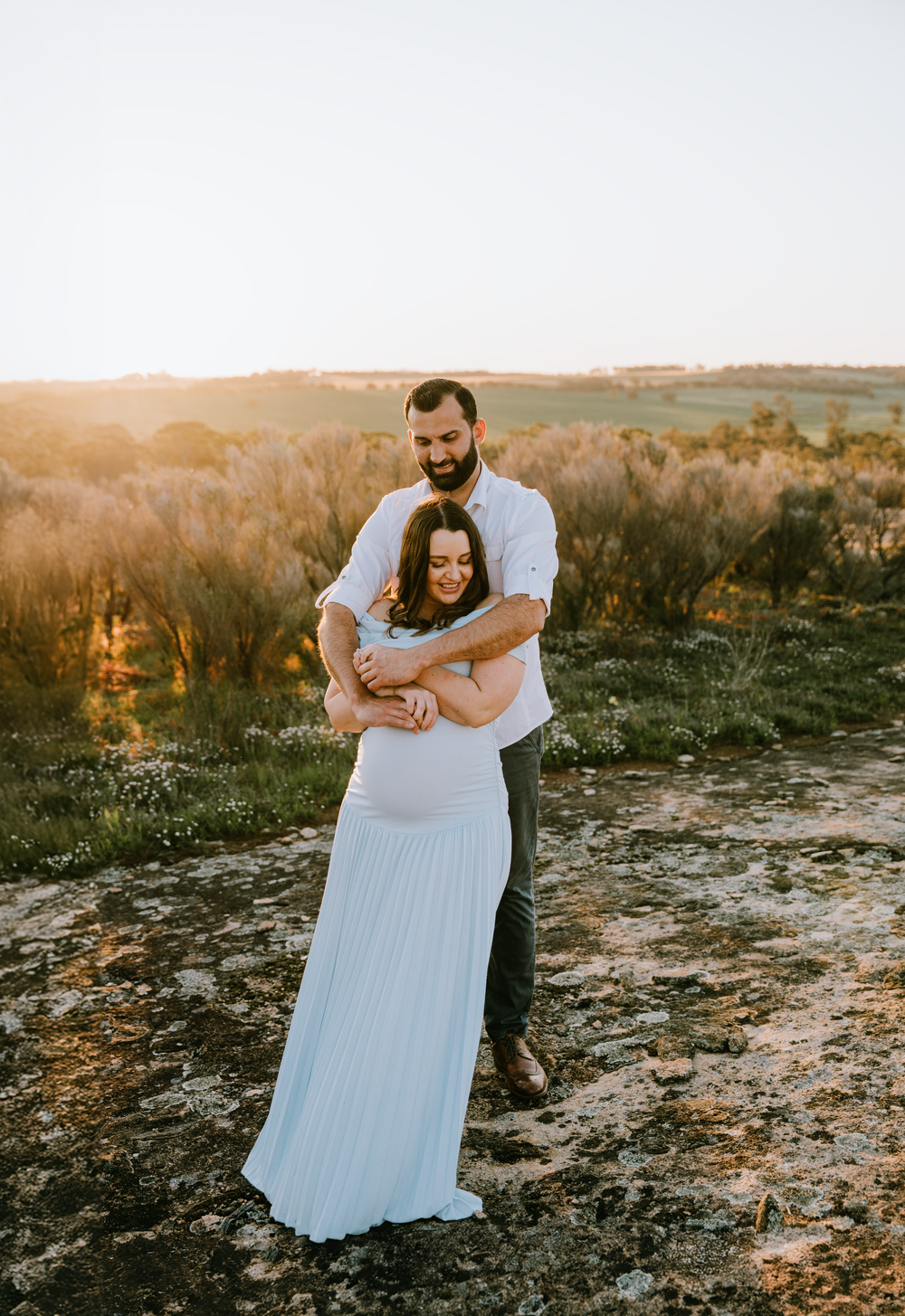 A couple shares an intimate moment during sunset in a rustic outdoor setting.