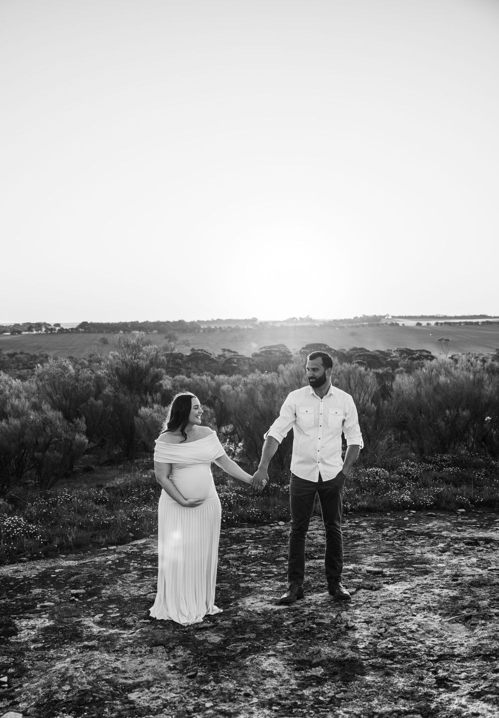 A black and white portrait of a couple standing together in a natural landscape.