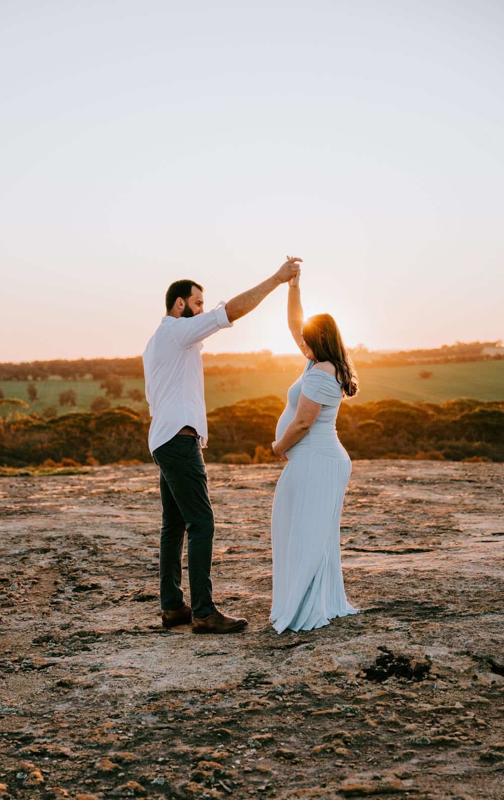 A couple dances together against a golden sunset backdrop in a natural setting.
