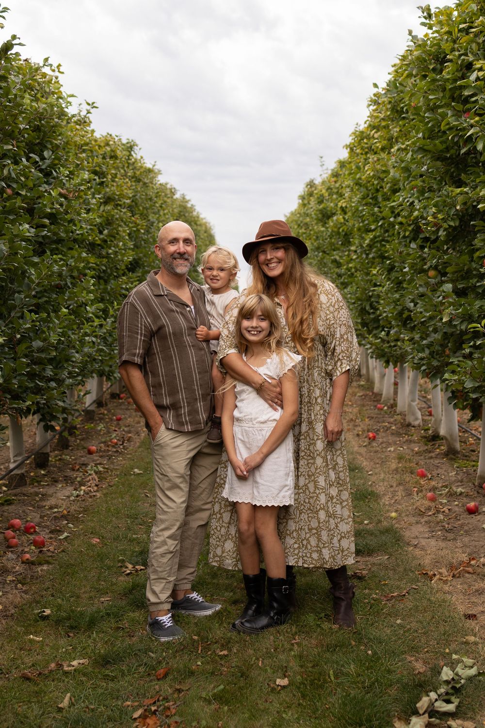 A family poses together between rows of fruit trees in an orchard on an overcast day at Shuh Orchards