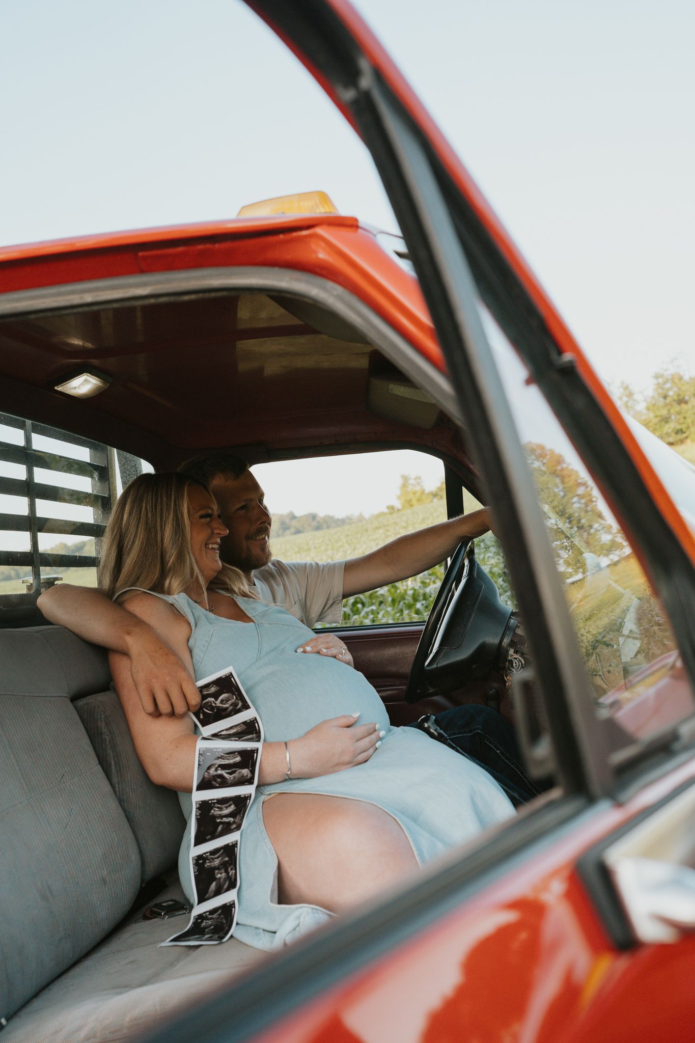 Couple sharing intimate moments inside a vintage red truck while looking at ultrasound photos. Jackson MI photography.
