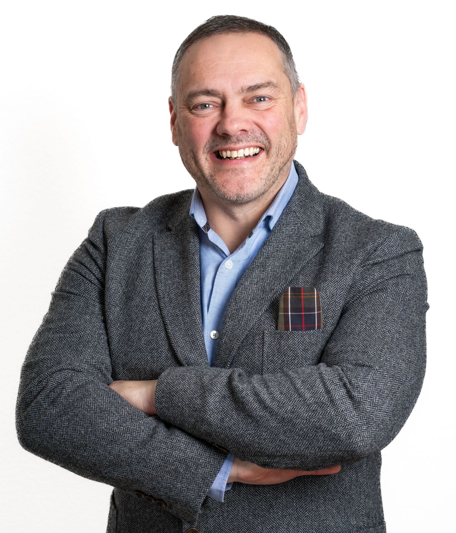 Professional headshot of businessman wearing grey blazer with plaid pocket square.