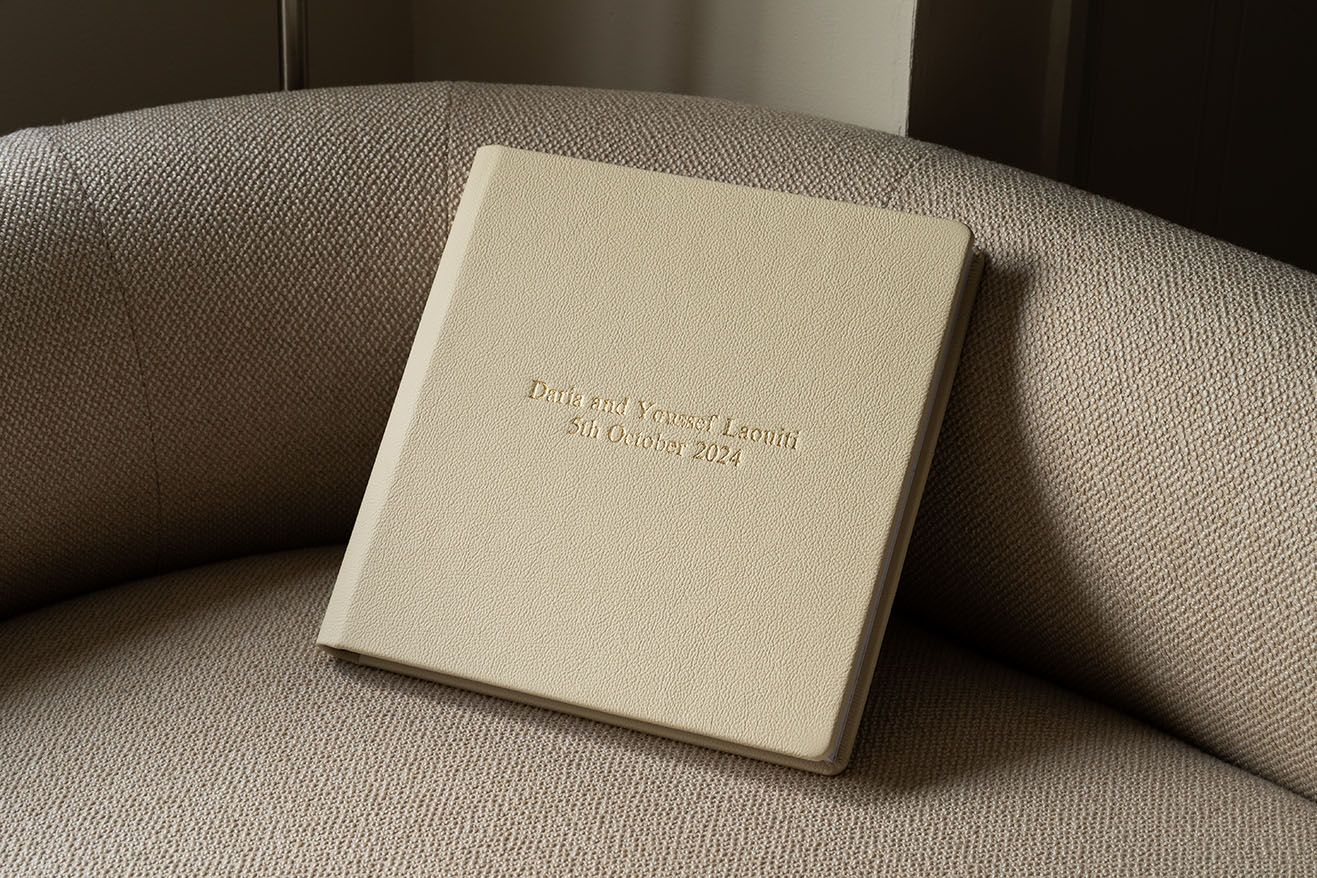 Elegant cream-colored book album with embossed text resting on a light beige leather couch.