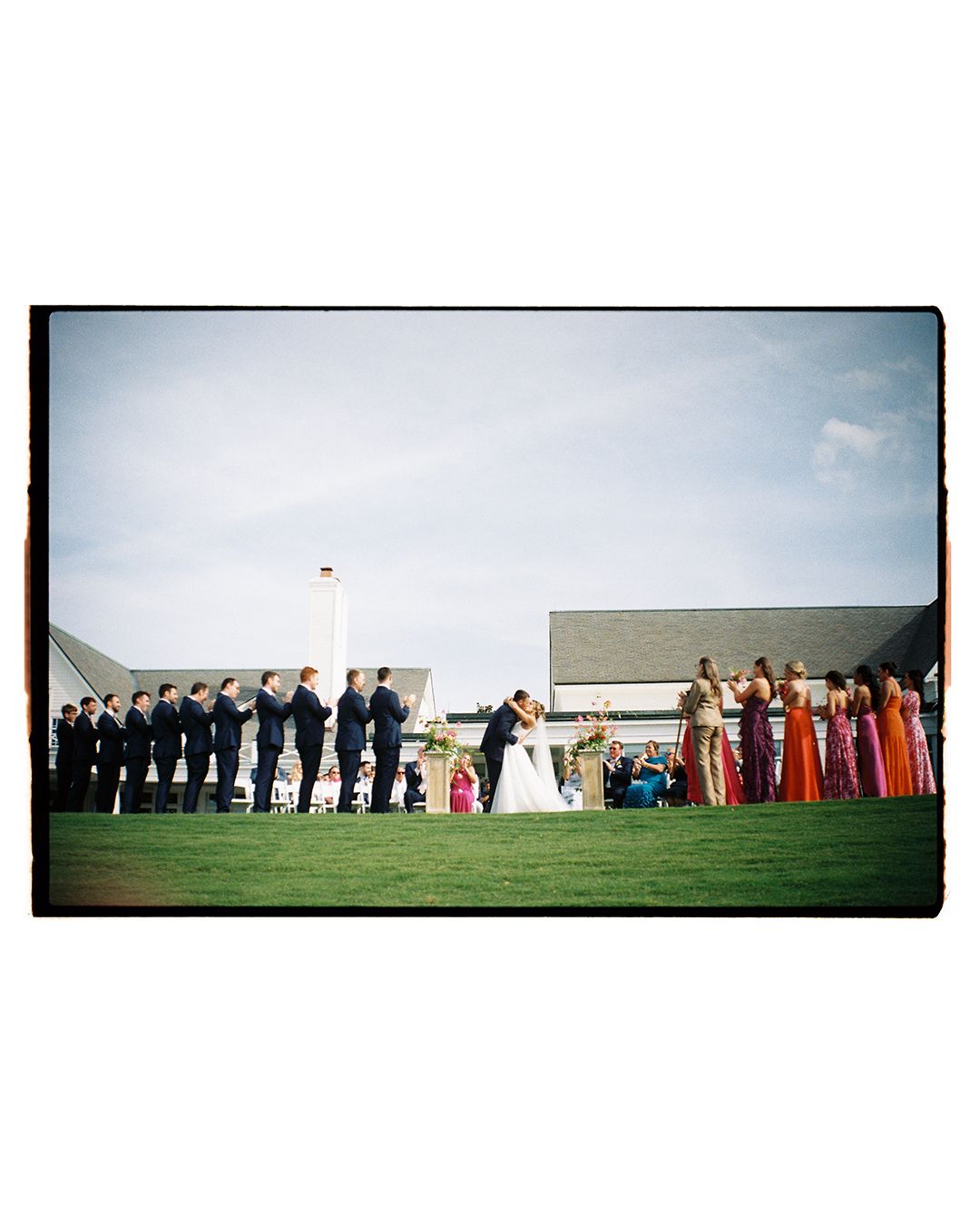 Wedding party lines up for a panoramic group photo on a grassy hillside.