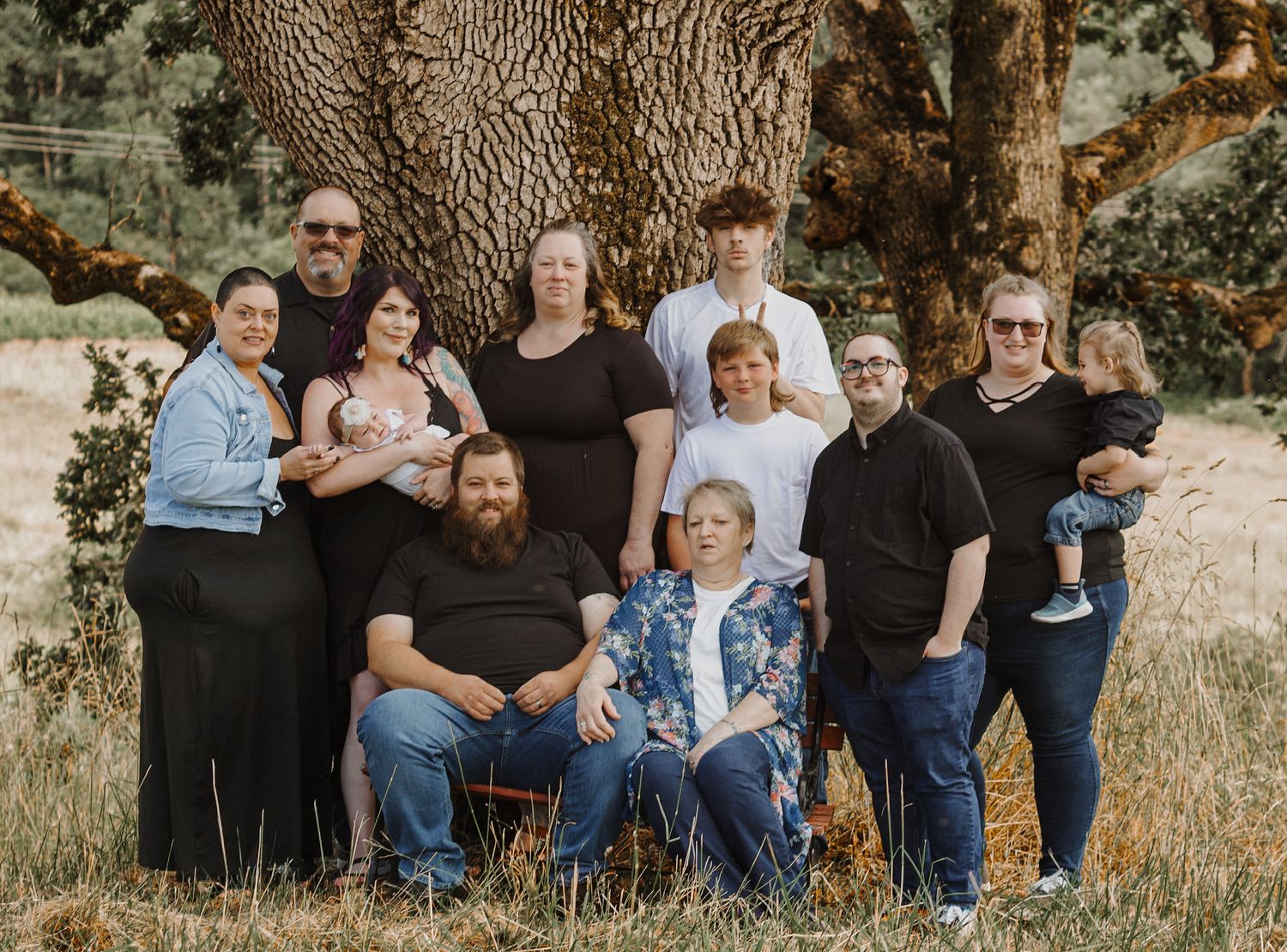 Large family portrait of ten people posing outdoors under a massive oak tree in a grassy field.