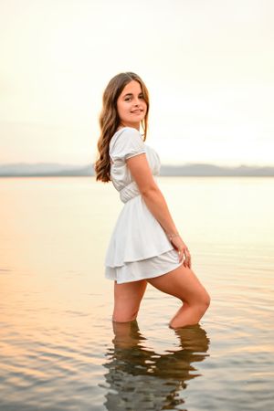 Artistic sunset portrait in water wearing white dress with warm golden tones.