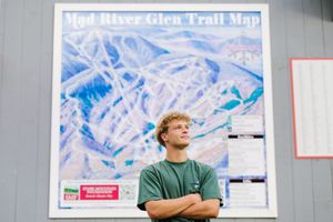 Someone stands with arms crossed in front of a large trail map showing mountain terrain at Mad River Glen ski resort.