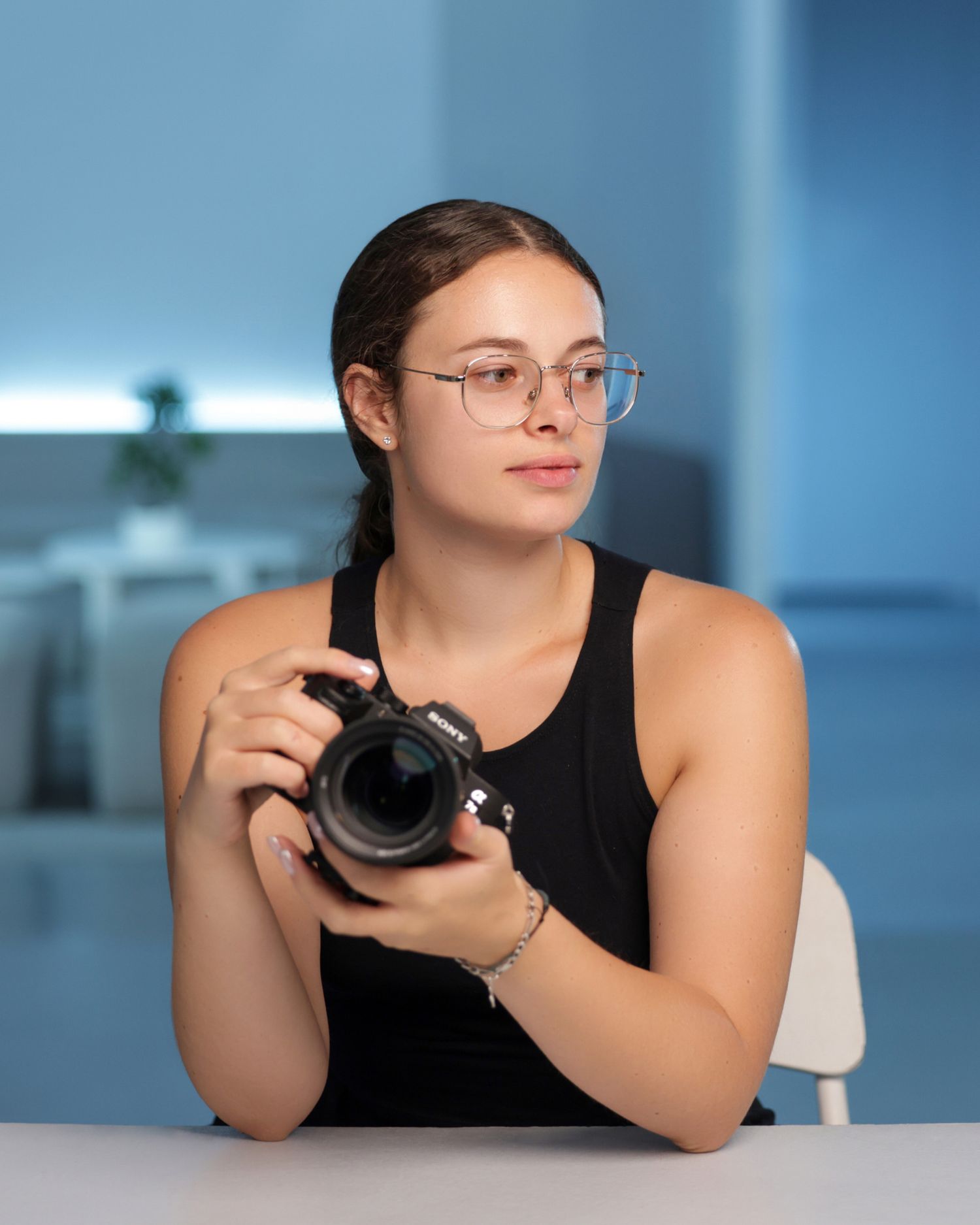 Photographer in black tank top reviews images on professional camera in blue-tinted studio.