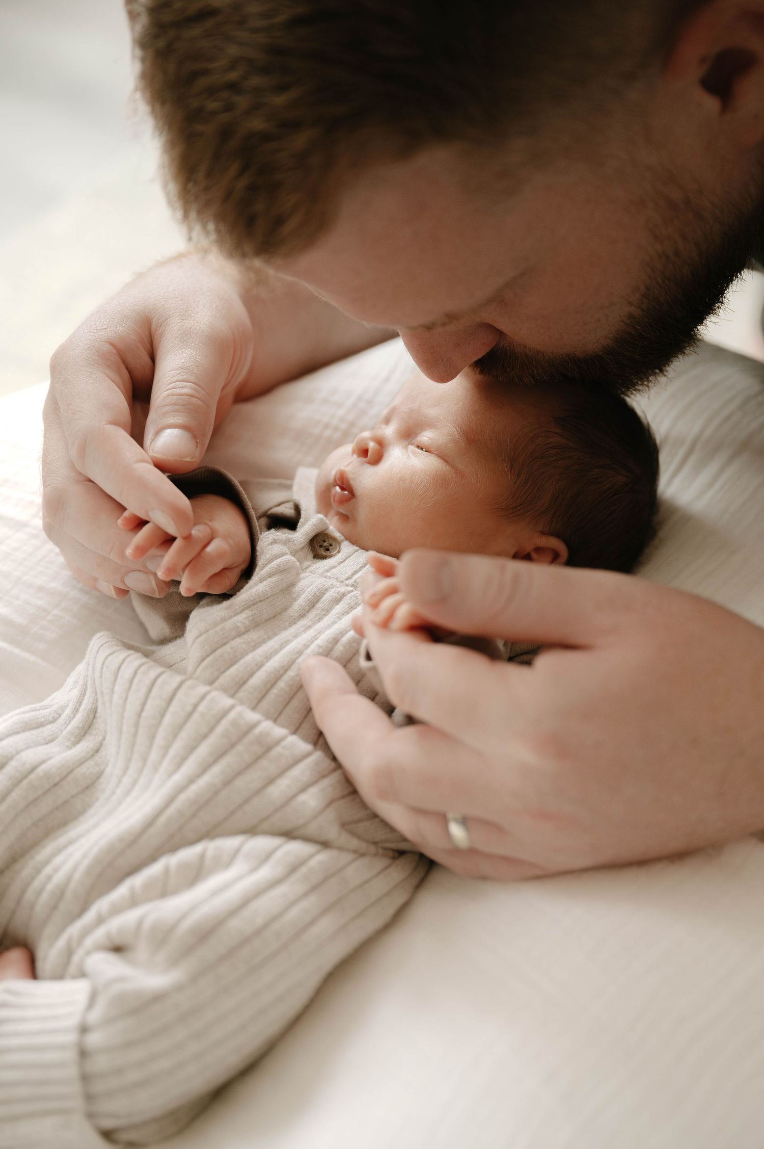 A tender moment captured in black and white as a gentle hand touches an infant lying on soft bedding.
