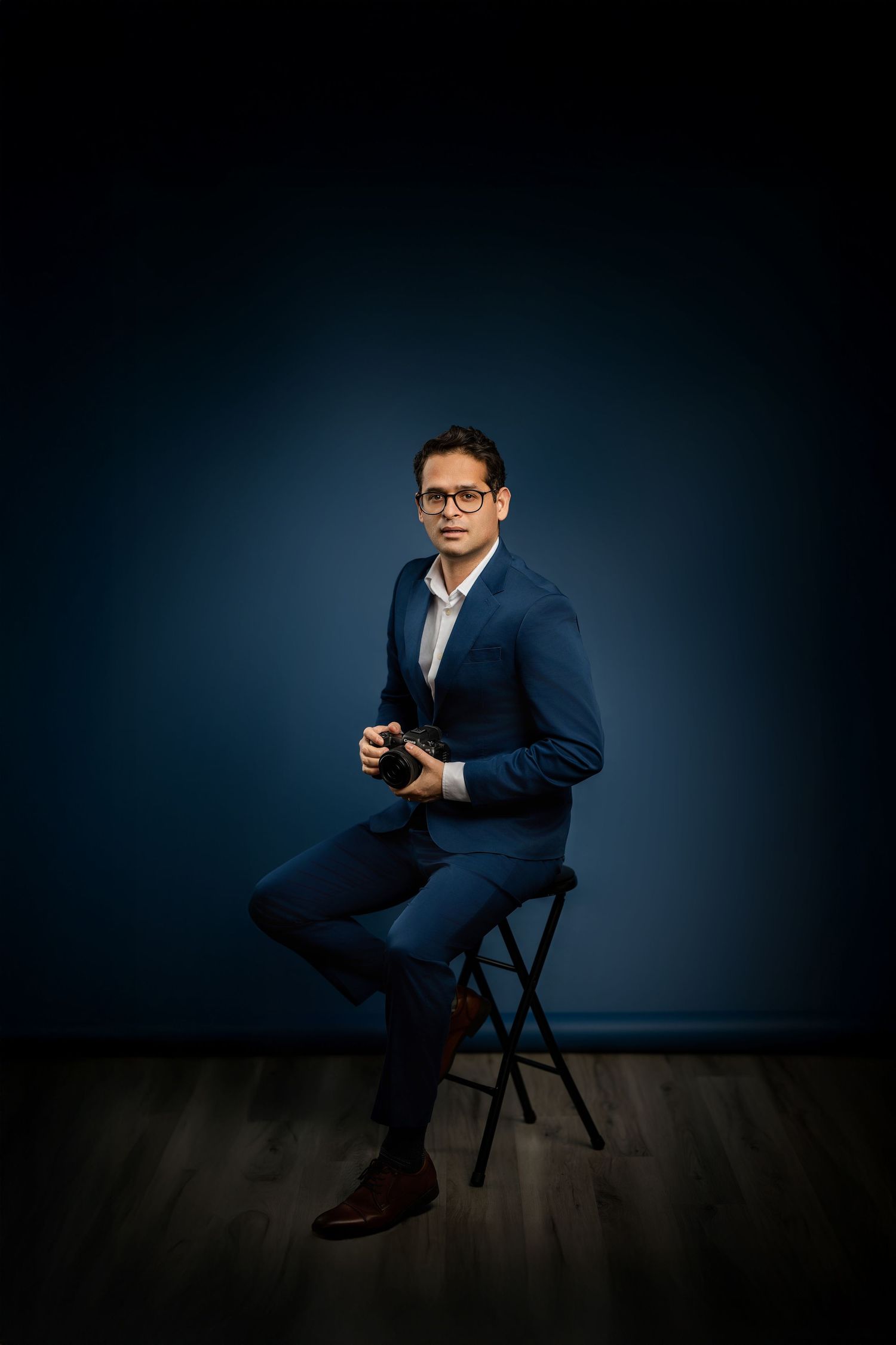 Professional studio portrait of a person in a navy suit against a dark blue backdrop.