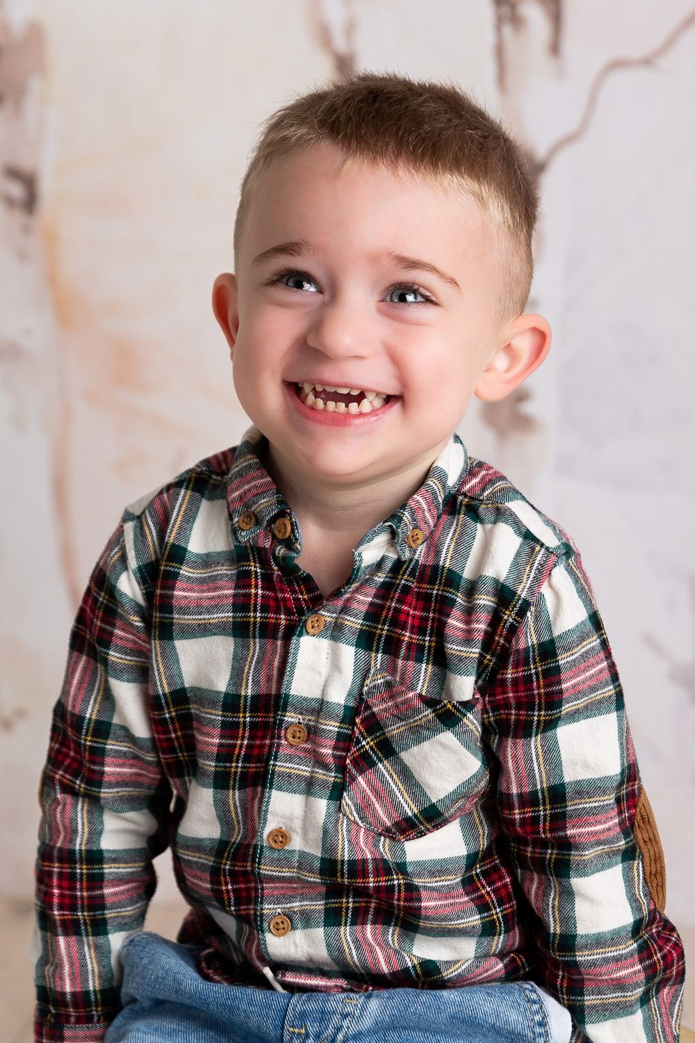 A child wearing a plaid flannel shirt and jeans smiles brightly in a studio photo series.