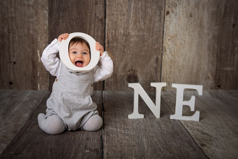 A series of baby milestone photos showing a baby in white clothing against a rustic wooden backdrop.