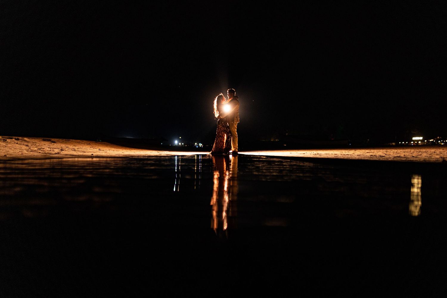 Silhouetted figure stands on beach at night with light creating dramatic reflection.