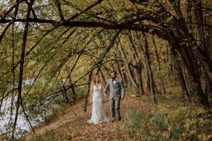 Mariés marchant main dans la main en forêt à l’automne au Québec, capturés par une photographe de mariage.