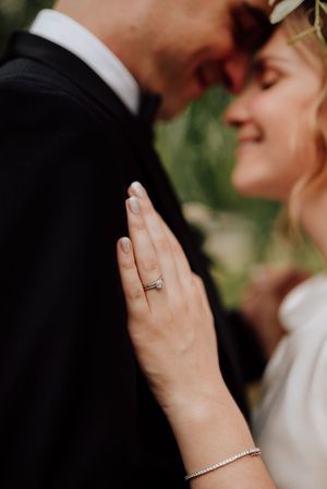 Détail de la bague de mariage sur la main de la mariée lors d’un moment complice capturé en gros plan.
