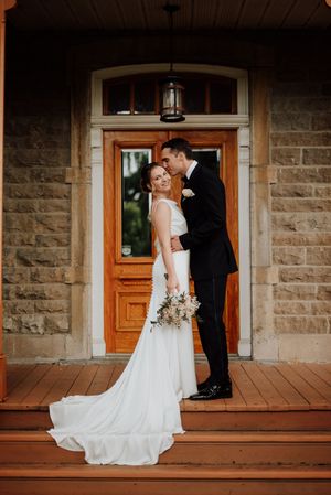 Photo élégante d’un couple le jour de leur mariage, devant une bâtisse en pierre typique du patrimoine québécois.