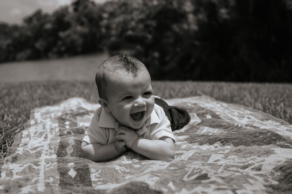 A black and white photo of a laughing baby laying on a blanket outdoors.