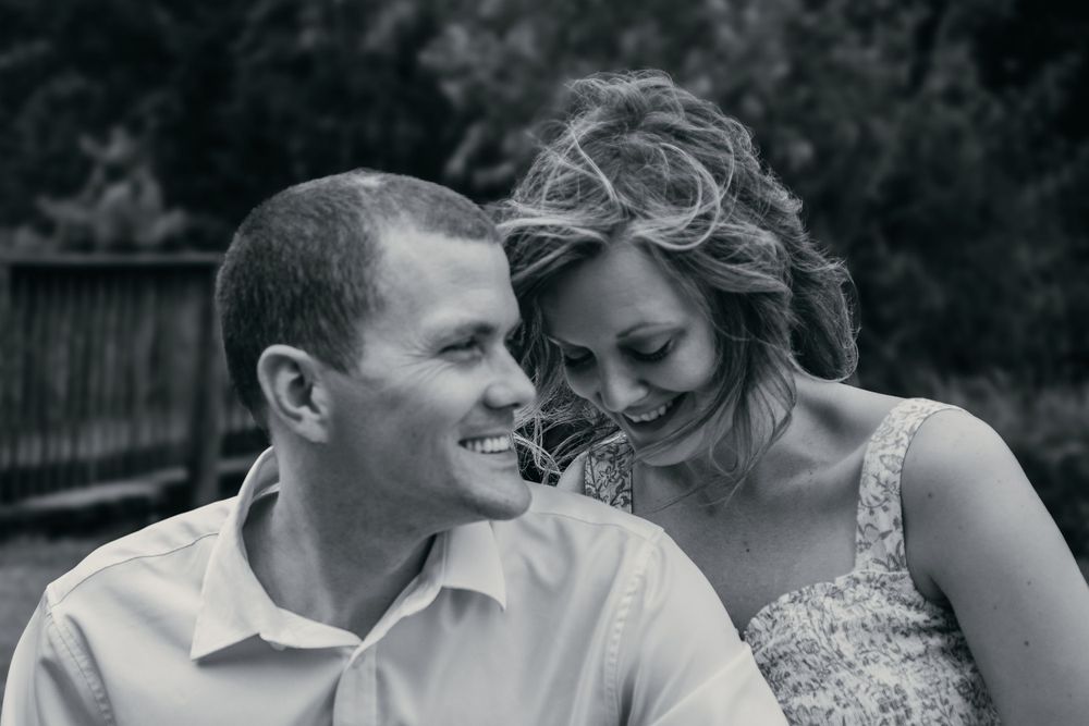 A black and white candid moment captured of a couple dressed in white sharing a joyful laugh.