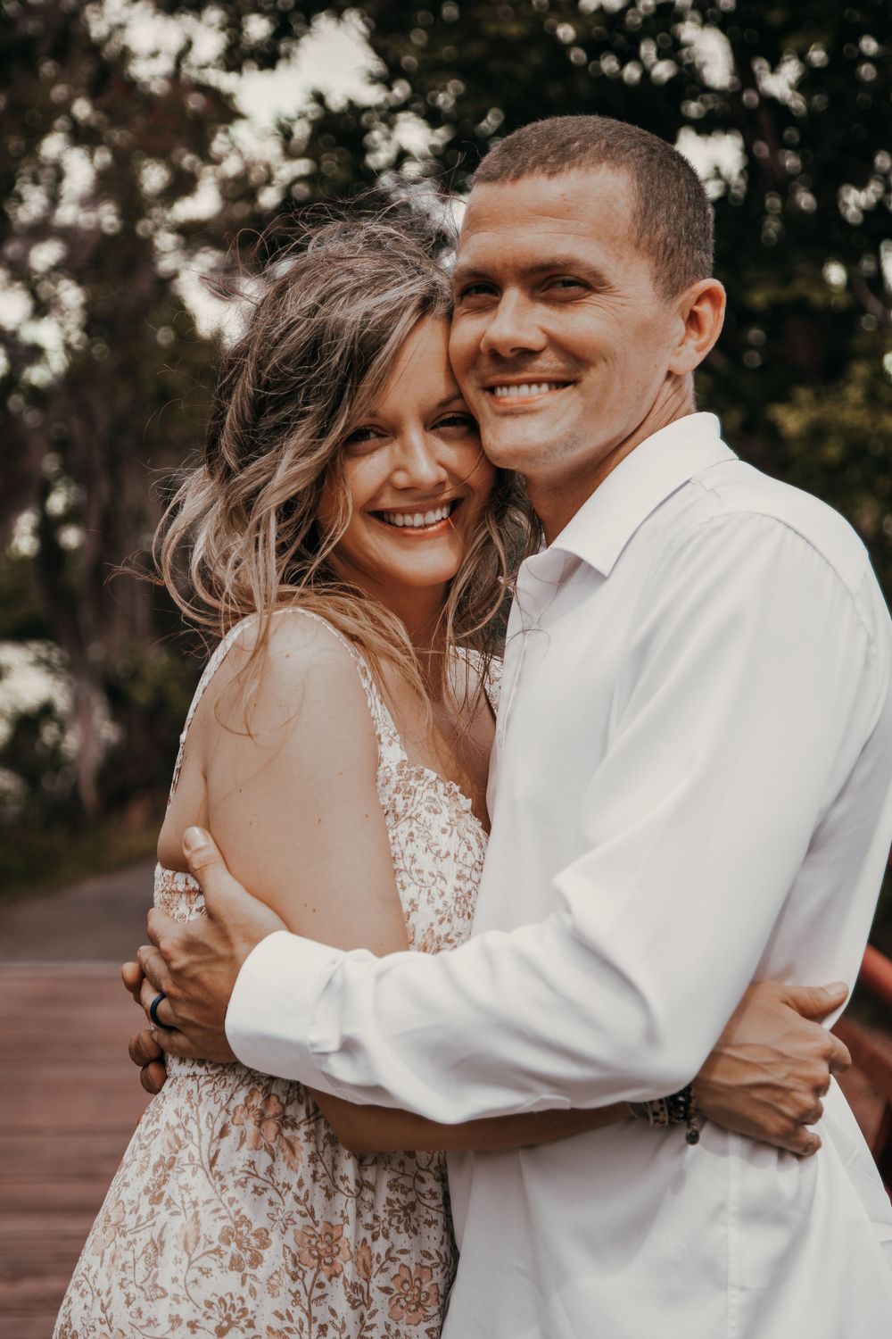 A romantic portrait of a couple embracing on a wooden deck, dressed in formal white attire.