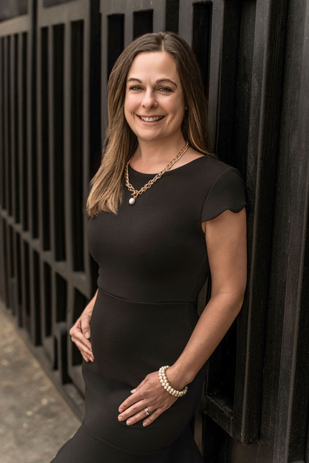 Professional portrait of someone in a black scalloped dress smiling against dark industrial background.