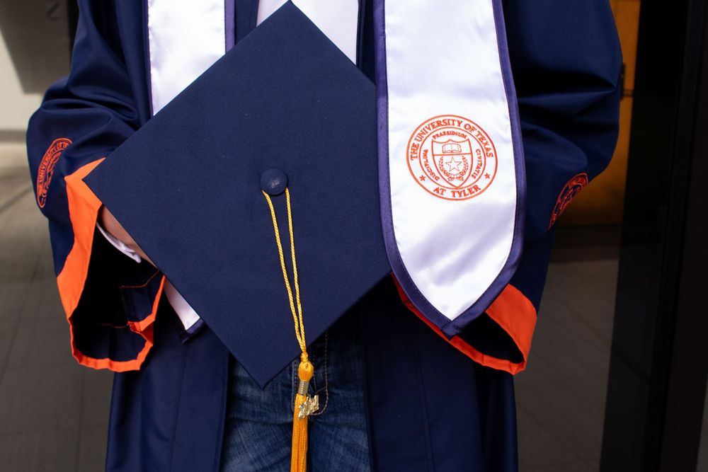 A graduation ceremony with graduates wearing navy blue gowns and orange accents standing in a line.