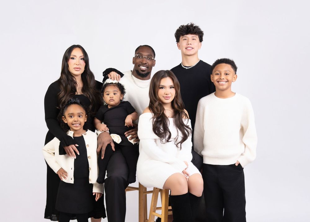 A group of people wearing black and white outfits pose together in a minimalist studio setting.
