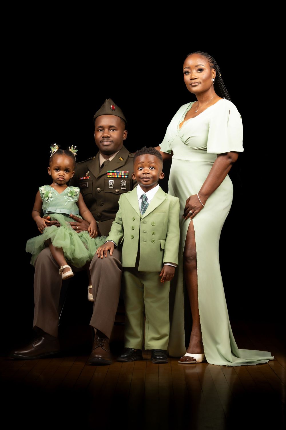 A family portrait against a dark background featuring military dress uniform and matching mint green outfits.