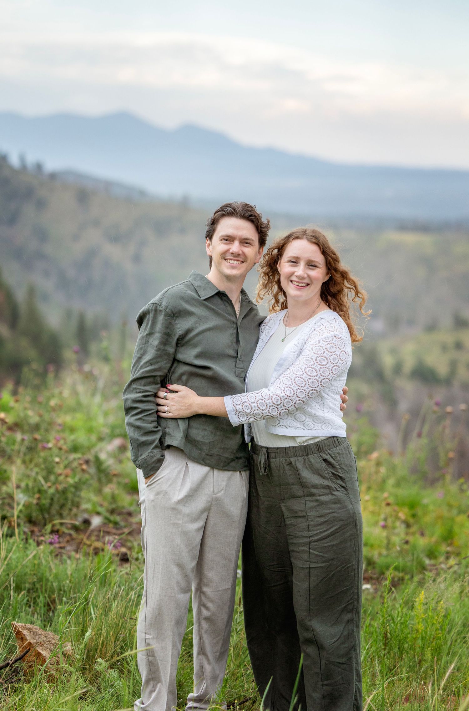 Couple shares a romantic moment kissing in a lush green forest during an outdoor engagement session.