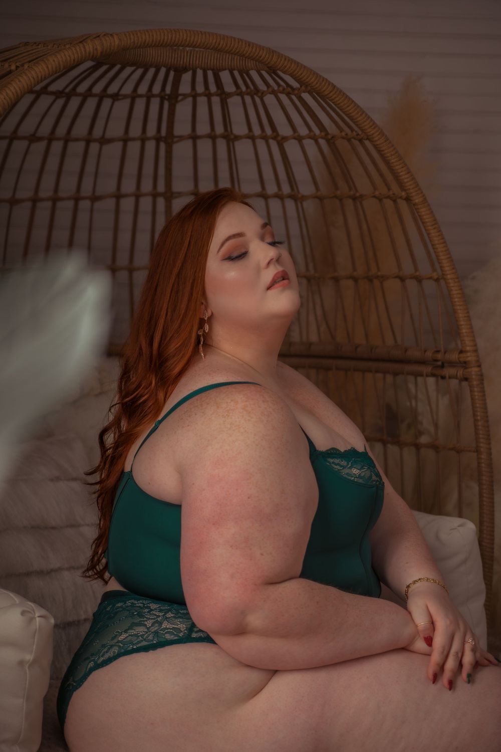Artistic boudoir photo in emerald green lingerie with a woven rattan chair frame in the background.