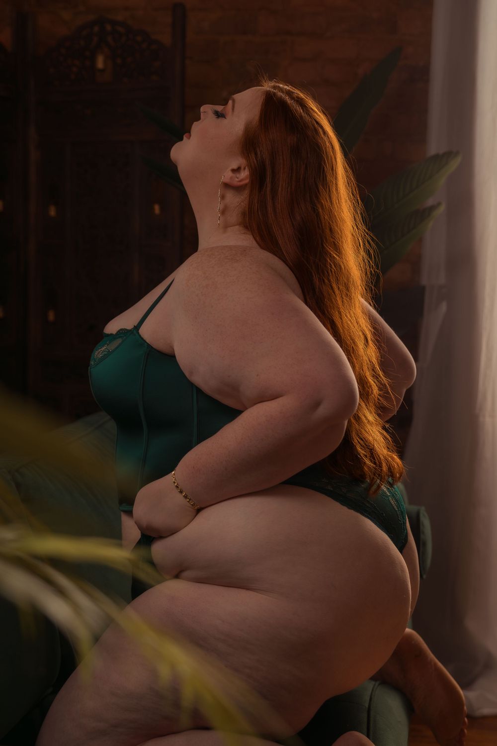 A person wearing a green swimsuit poses confidently with sunlit hair in an intimate boudoir photography setting.