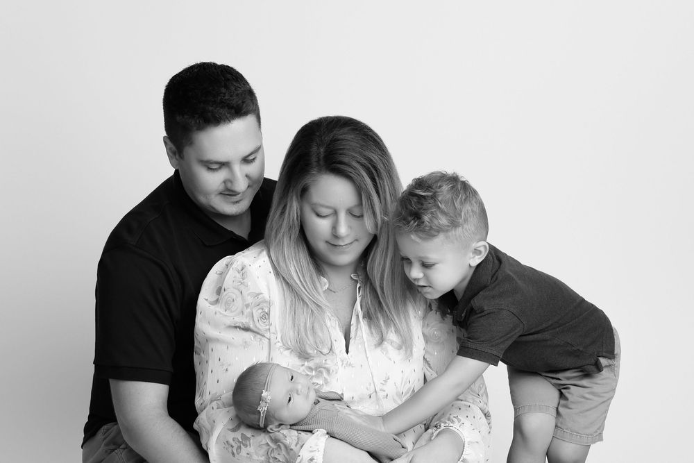 Black and white family portrait with parents and two children, one a newborn, sharing a tender moment in Covington, GA