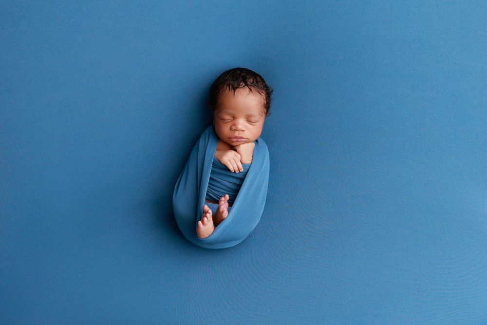 Sleeping newborn baby wrapped snugly in a blue swaddle on a matching blue background. photographer covington, ga