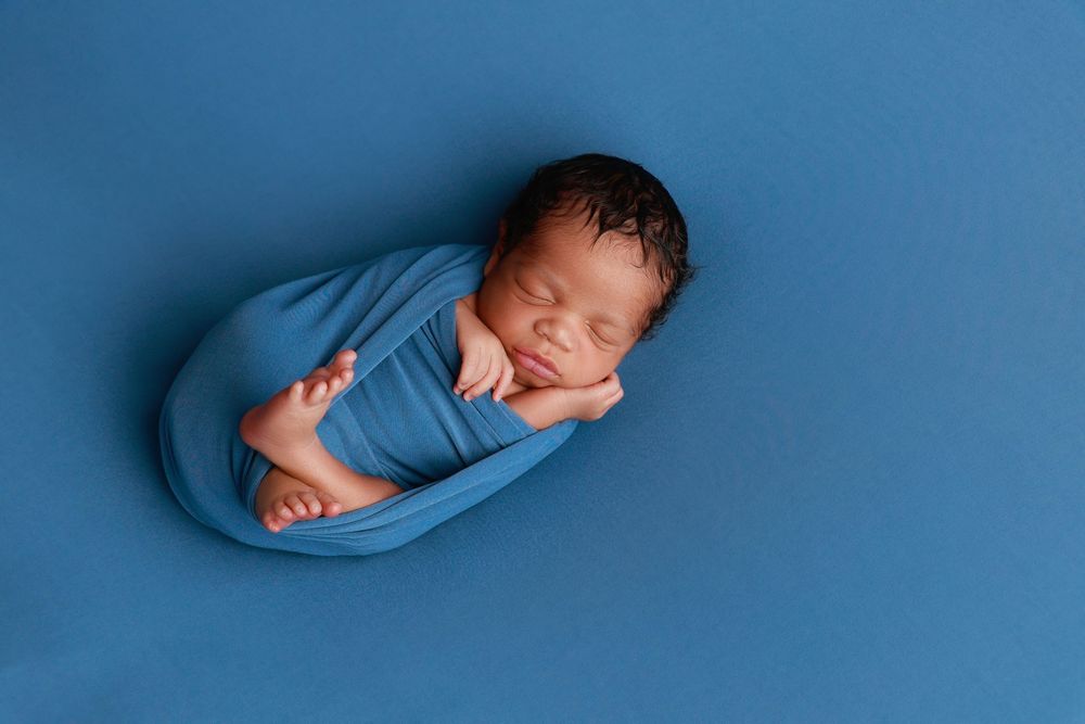 Peacefully sleeping newborn wrapped in blue swaddle cloth posed on a blue backdrop. photographer covington, ga