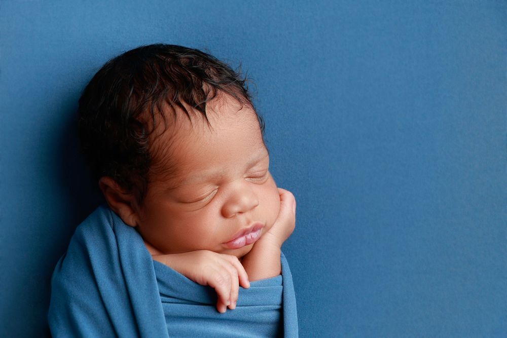 Close-up of a sleeping newborn baby wrapped in a blue swaddle with hands near face. photographer covington, ga
