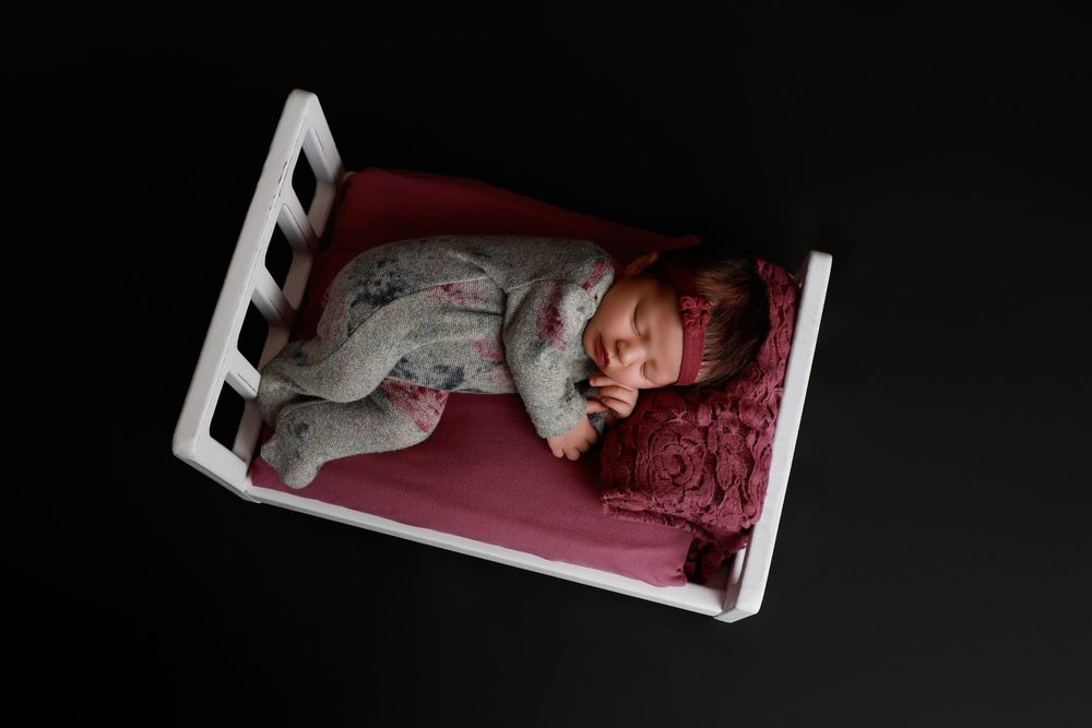 Newborn baby in gray floral onesie sleeping in small white wooden crib with pink bedding. photographer covington, ga