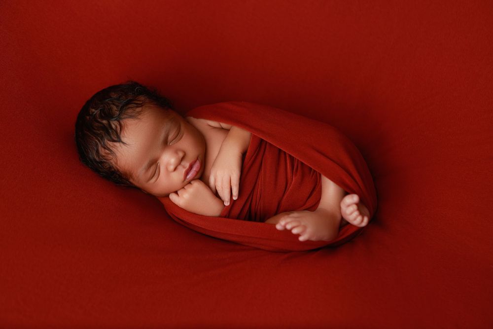 Smiling sleeping newborn baby wrapped in red swaddle cloth on a red background. photographer covington, ga
